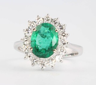 An 18ct white gold oval emerald and diamond cluster ring, the centre stone approx. 2.0ct, the brilliant cut diamonds 0.69ct, size M 1/2