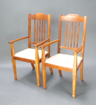 A pair of Arts & Crafts Liberty style oak stick and rail back carver chairs with upholstered seats raised on square tapered supports 