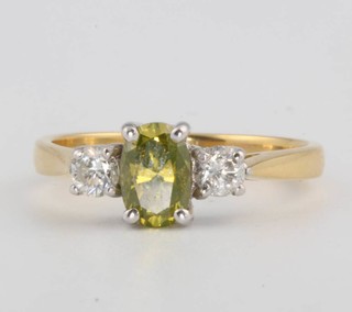 An 18ct yellow gold ring, the centre treated oval cut green yellow diamond approx. 0.65ct flanked by brilliant cut diamonds approx. 0.15ct size N, complete with EDR certificate 