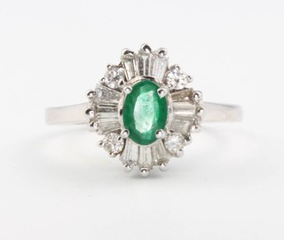 An 18ct white gold emerald and diamond cluster ring, the oval centre stone surrounded by tapered baguette and brilliant cut diamonds, size L 