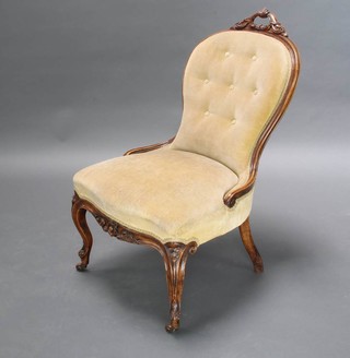 A Victorian walnut show frame nursing chair with pierced scroll crest, raised on cabriole supports with ceramic castors with button back and upholstered in cream velour