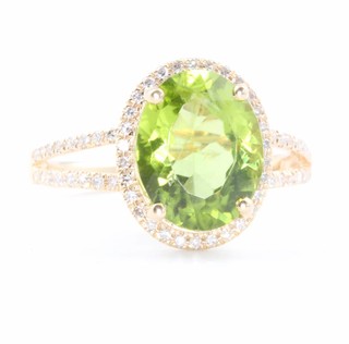 A 14ct yellow gold oval peridot and diamond cluster ring the centre stone 3.81ct surrounded by brilliant cut diamonds 0.25ct, size M 1/2