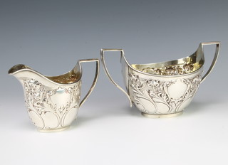 An Edwardian repousse silver sugar bowl and milk jug decorated with Iris, Sheffield 1903, 414 grams 