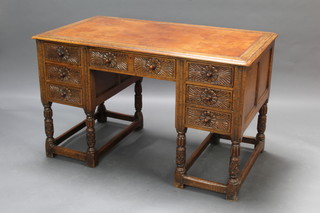 An Ipswich style carved oak desk with tan inset writing surface above 1 long and 6 short drawers, heavily carved throughout, raised on cup and cover supports 74cm h x 121cm w x 69cm d 