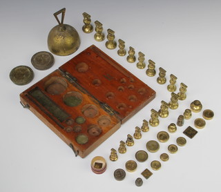 A collection of brass weights comprising two circular 4 oz, seven 1/2 oz weights, four circular 1/4 oz weights, three  2 oz bell weights, ten 1 oz bell weights, five  1/2 oz bell weights together with seven other weights, a weight box and a brass table bell  