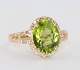 A 14ct yellow gold oval peridot and diamond cluster ring the centre stone 3.81ct surrounded by brilliant cut diamonds 0.25ct, size M 1/2