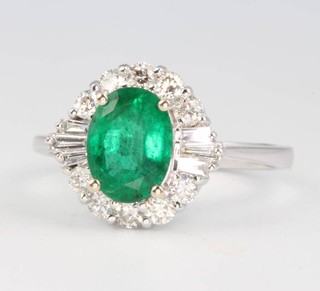 An 18ct white gold emerald and diamond cluster ring, the centre oval stone 1.29ct surrounded by brilliant and baguette cut diamonds 0.51ct, size N 