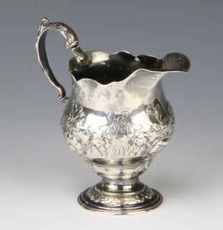 A George III silver cream jug with repousse floral decoration and monogram having an S scroll handle, London 1761, 134 grams 
