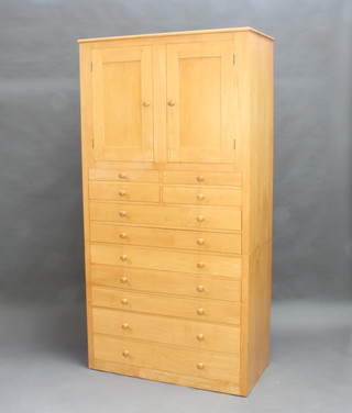 A beech press cabinet, the upper section with cupboard enclosed by double panelled doors, the base fitted 4 short drawers above 7 long drawers with tore handles, raised on a platform base 198cm x 102cm w x 51cm d (1 handle is f and r)  