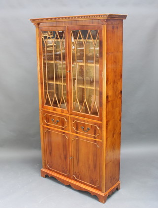 A Georgian style yew display cabinet, the upper section with moulded and dentil cornice, the shelved interior enclosed by astragal glazed panelled doors, the base fitted 2 long drawers above a double cupboard with fluted columns to the sides 191cm h x 103cm w x 36cm d  
