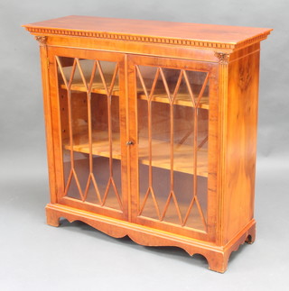 A Georgian style yew bookcase with moulded and dentil cornice, fitted adjustable shelves and with columns to the sides enclosed by astragal glazed panelled doors 97cm x 102cm w x 37cm d 