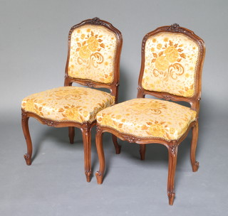 A pair of French carved oak show frame salon chairs, the cresting rails carved roses, the seats and backs upholstered in yellow material raised on cabriole supports 