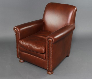 A club style armchair upholstered in brown leather raised on bun supports 