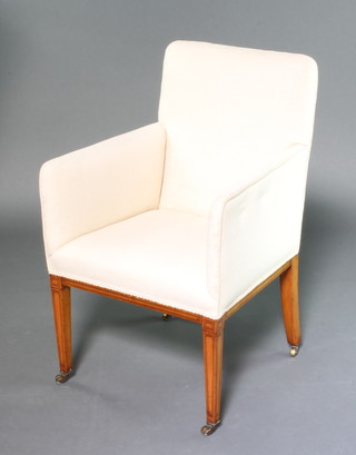 An Edwardian inlaid mahogany armchair, the seat and back upholstered in white material raised on square tapered supports ending in brass caps and casters 