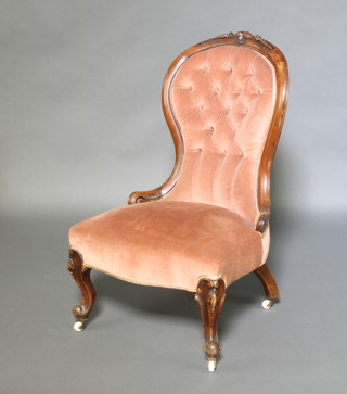 A Victorian mahogany carved show frame nursing chair the seat and back upholstered in pink buttoned dralon, raised on cabriole supports