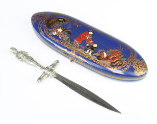 An Art Deco double bladed paper knife with 11 cm blade, the grip in the form of a standing Joan of Arc contained in an oval chinoiserie style spectacle case the interior marked Theodore Hamblin Ltd 