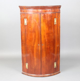 A Georgian mahogany bow front hanging corner cabinet, fitted 3 shelves and 3 drawers to the base enclosed by panelled doors with brass H framed hinges 121cm h x 70cm w x 49cm d 