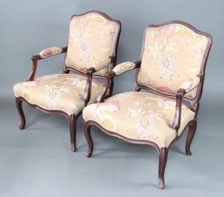A pair of French carved mahogany show frame open arm salon chairs the seats and backs upholstered in floral material raised on cabriole supports 