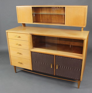 In the manner of Gordon Russell, a mid 20th Century light teak sideboard, the raised back fitted a cupboard enclosed by glazed and panelled oak doors, the base fitted 4 long drawers flanked by a cupboard enclosed by a glazed panelled door above a cupboard enclosed by a panelled door with lattice style decoration 124cm h x 130cm w x 45cm d 