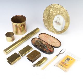 An Art Nouveau style circular brass photograph frame decorated a classical lady 15cm, a cylindrical brass and copper vase 8cm x 8cm, 2 WWI brass match slips, 2 brass cased lighters, a copper and brass napkin ring, a pickle fork, a cylindrical brass case formed from a shell case containing a fan, a pair of gold scales and a 1940's packet of Top Hat cigarettes
