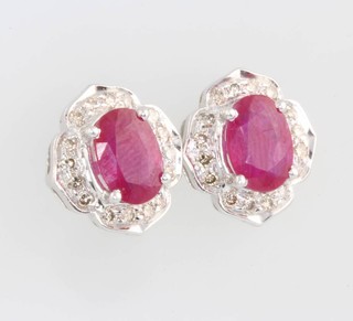 A suite of 14ct white gold ruby and diamond jewellery comprising a cluster ring size N, a pair of ensuite ear studs and a pendant 