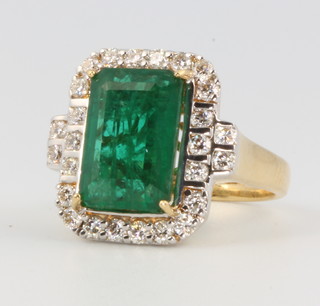 An 18ct yellow gold emerald cut emerald and diamond cluster ring, the centre stone 6.92ct surrounded by brilliant cut diamonds 4.94ct, size N 