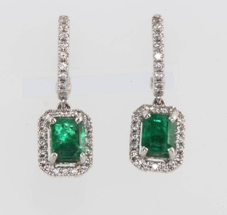 A pair of 18ct white gold emerald and diamond earrings, the emerald cut centre stones approx. 0.99ct surrounded by brilliant cut diamonds 0.28ct