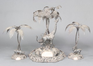 A Victorian silver plated table centre piece by Elkington & Co with a giraffe, emu and deer beneath palm trees on a rocky base on a mirrored rustic base 61cm h together with a pair of ensuite smaller ditto decorated with deer 46cm h