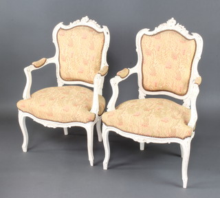A pair of 19th Century white painted French open arm salon chairs with upholstered seats and backs, raised on cabriole supports 