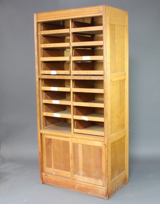 A 1930's Art Deco light oak drapers display cabinet with moulded cornice, the upper section fitted 15 shallow trays the base fitted a cupboard enclosed by a sliding panelled door 198cm h x 92cm w x 53cm d 