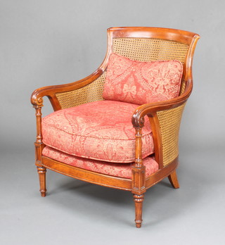 A Georgian style beech double cane tub back bergere armchair with upholstered seat raised on turned supports 
