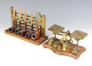 A pair of brass postage scales complete with weights raised on an oak base and an oak and brass pipe rack in the form of a 5 bar gate and 5 pipes