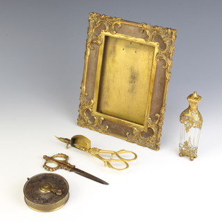 A gilt metal mounted easel photograph frame 20cm x 16cm, a 19th Century faceted glass and pierced gilt metal mounted scent bottle 12cm x 3cm x 2cm, a pair of gilt metal candle snuffers, ditto scissors and a gilt metal and silver tape measure (dented)