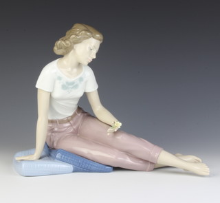 A Nao figure of a lady sitting on a cushion holding a flower 24cm 
