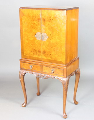 A Queen Anne style figured walnut cocktail cabinet with quarter veneered and crossbanded top above a cupboard enclosed by a panelled door, the base fitted 2 short drawers raised on cabriole supports 138cm x 63cm x 41cm 