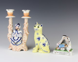 A Galle style ceramic figure of a cat with glass eyes 15cm, a fairing and a bisque 2 light candle holder with a seated figure with nodding head 