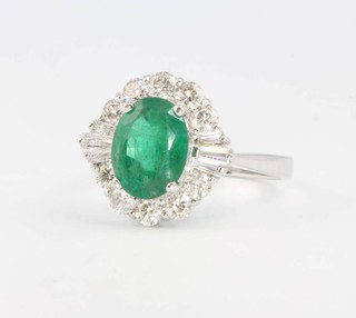 An 18ct white gold oval cut emerald and diamond cluster ring, the oval cut stone approx 1.97ct surrounded by brilliant and tapered baguette cut diamonds approx. 0.91ct size M 