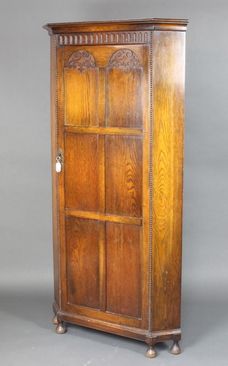 A 1930's carved oak corner wardrobe with moulded cornice, arcaded and panelled door, raised on bracket feet 175cm h  x 88cm w x 56cm 