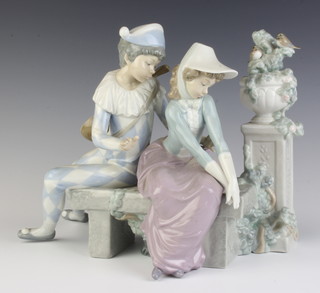 A Nao figure of a harlequin sitting with a young lady on a bench beside a column with an urn and birds 25cm 