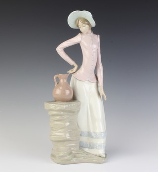 A Nao figure of a lady standing beside a plinth with a ewer 35cm 