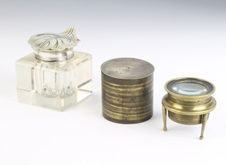 A Victorian square glass inkwell with silver plated leaf shaped lid 4cm x 5cm x 5.5cm, a 19th Century circular table magnifying glass contained in a cylindrical case the top marked Tryme 