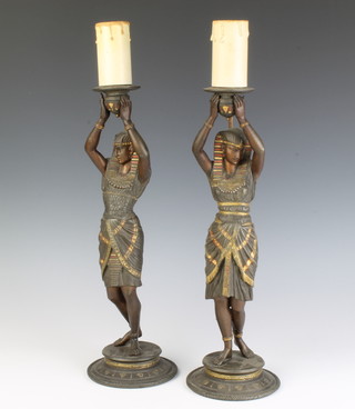 A pair of spelter table lamps in the form of standing Egyptian ladies possibly converted from candlesticks, raised on circular bases, 38cm 