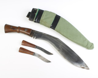 A military style Kukri, the 31cm blade with broad arrow marked India, complete with 2 skinning knives and contained in a leather and green canvas scabbard 
