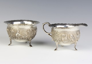 An Indian repousse silver cream jug and sugar bowl decorated with figures before buildings in a forest setting 303 grams