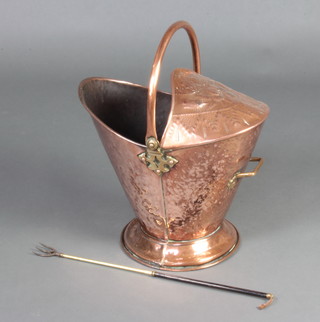 An Edwardian embossed copper and brass helmet shaped coal scuttle raised on a circular spreading foot and a brass and steel telescopic toasting fork 