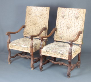 A pair of Italian style carved walnut open arm chairs, the seats and backs upholstered in tapestry, raised on shaped supports with H framed stretcher 