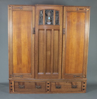 An Edwardian Liberty style Art Nouveau light oak double wardrobe with shaped cornice and lead glazed glass panel to the centre, flanked by a pair of cupboards enclosed by a pair of panelled doors, the base fitted 2 long drawers (it is possible that bracket feet have been removed) 183cm h x 168cm w x 44cm d 