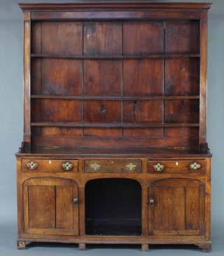 A Georgian oak dog kennel dresser, the raised back with moulded cornice fitted shelves, the base fitted 3 long drawers above a dog kennel recess flanked by a pair of arched panelled cupboards with replacement brass drop handles and ivory escutcheons 236cm h x 182cm w x 52cm d 