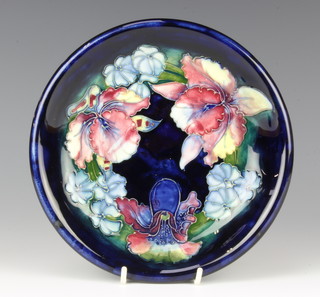 A William Moorcroft shallow bowl, the blue ground decorated with orchids, impressed and signature marks with attached label 23cm 