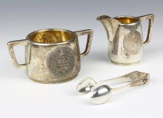 An Indian repousse silver 2 handled sugar bowl and cream jug together with a pair of sugar tongs decorated with deities 270 grams 